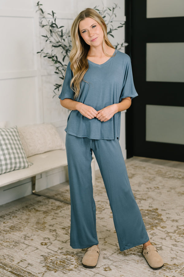 Woman wearing a blue outfit standing in a room with a plant and sofa.