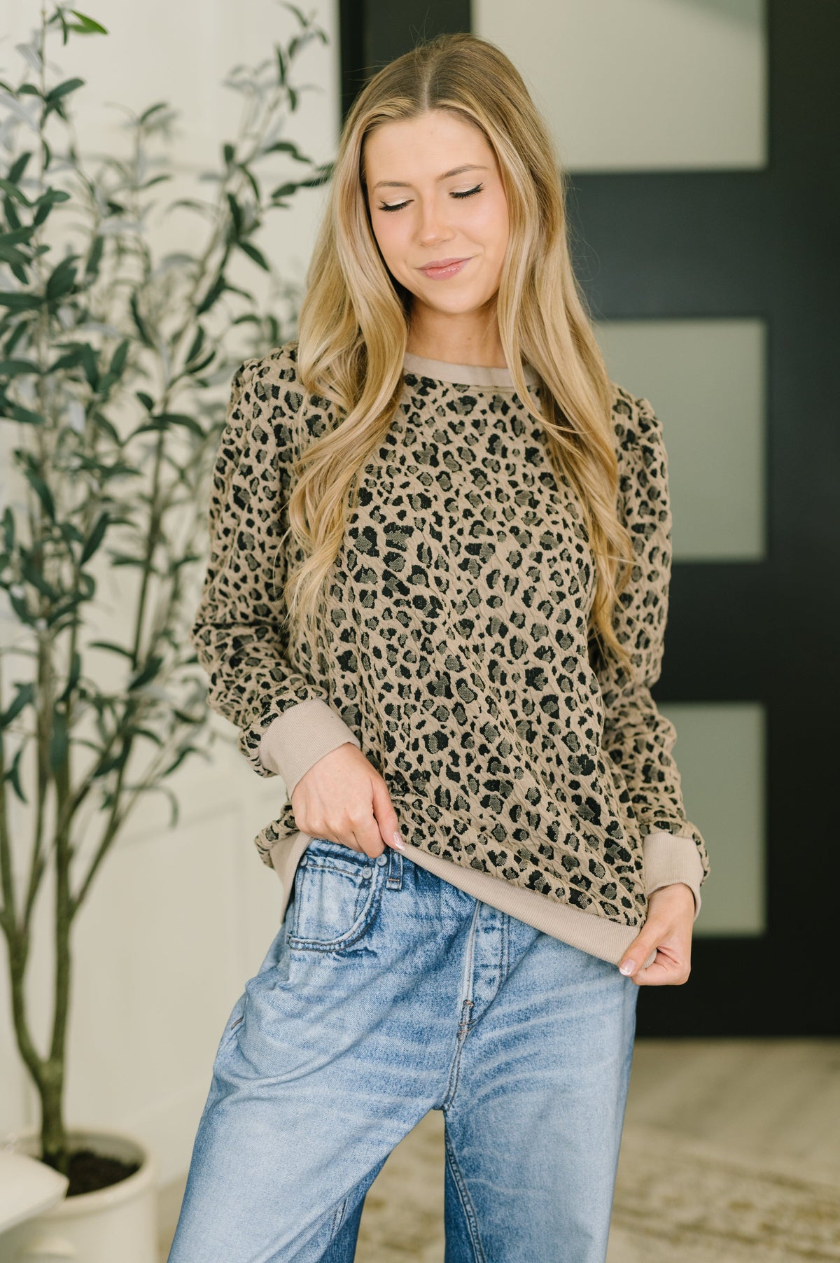 Woman wearing a leopard print sweater and blue jeans indoors.