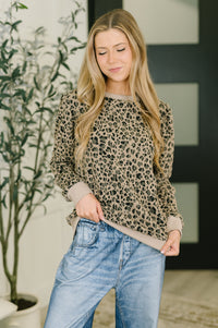 Woman wearing a leopard print sweater and blue jeans indoors.