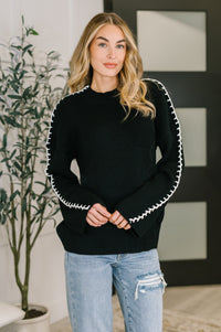 Woman wearing a black sweater with white trim in an indoor setting