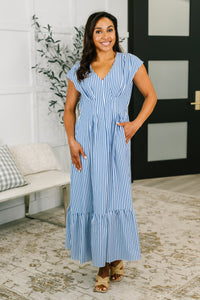 Woman wearing a blue and white striped dress standing in a room with a plant and bench.