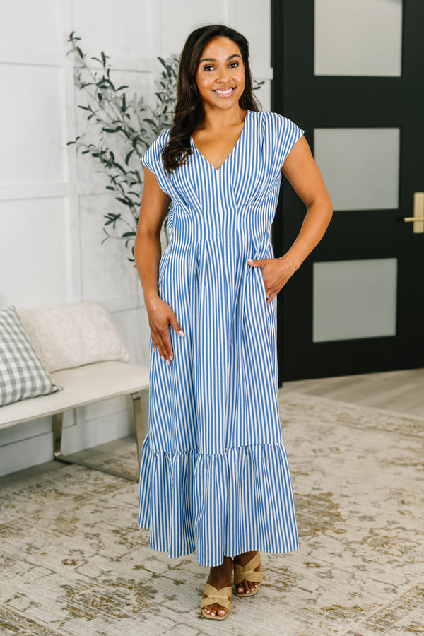 Woman wearing a blue and white striped dress standing in a room with a plant and bench.