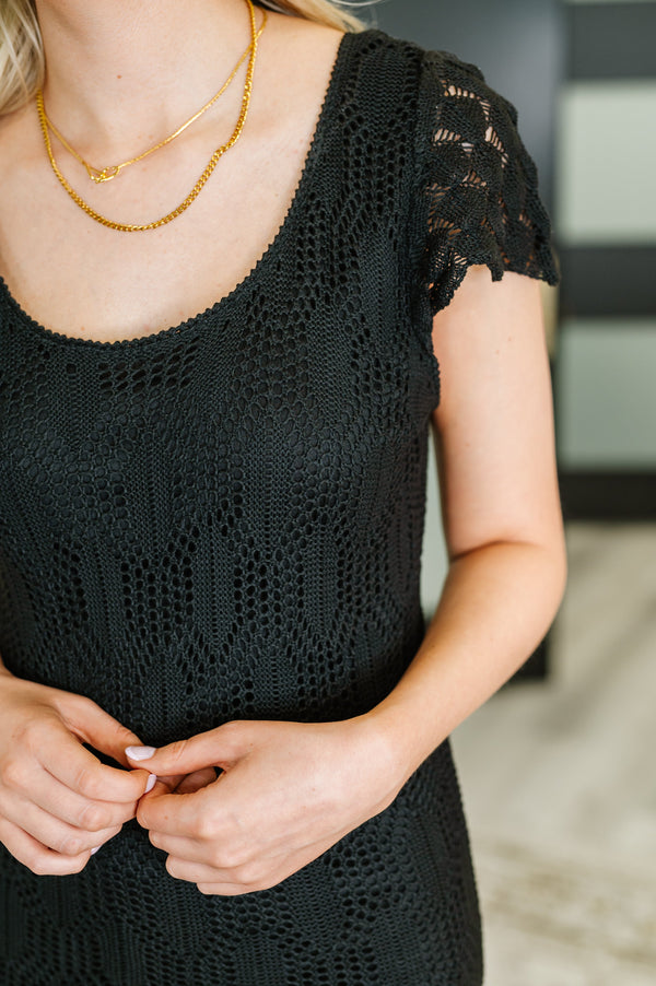 Person wearing a black lace dress with gold necklaces in an indoor setting