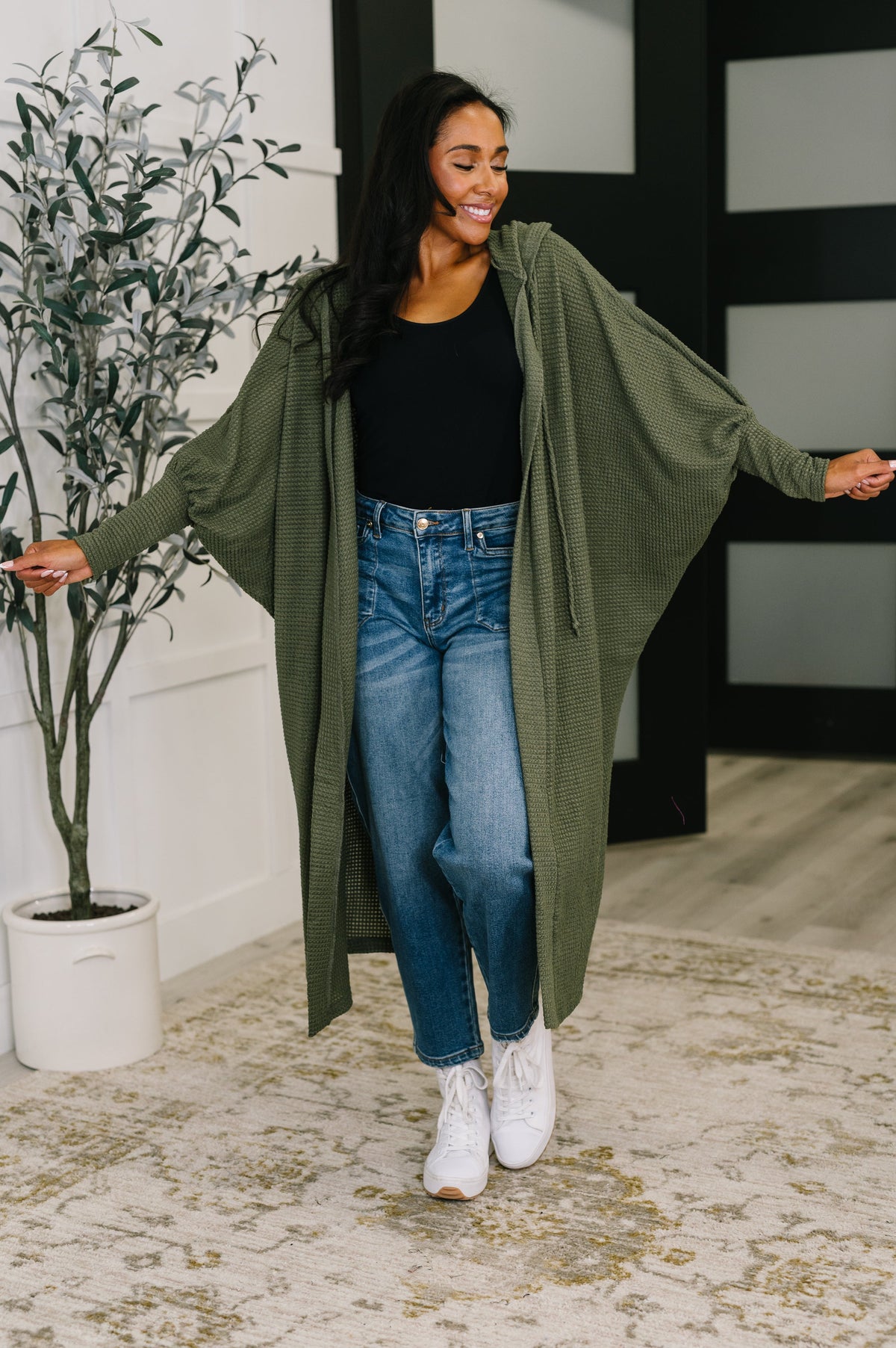 Woman wearing a green cardigan, black top, and blue jeans indoors.