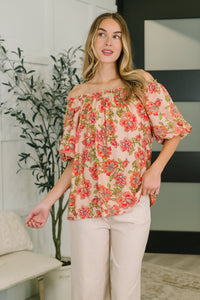 Woman wearing a floral off-shoulder top in a room with a plant and couch.