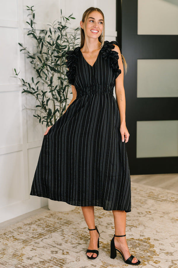 Woman wearing a black dress with ruffled sleeves in an indoor setting.