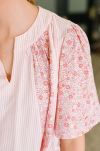 Close-up of a person wearing a blouse with a split neckline, featuring a light pink and white vertically striped panel on one side and a pink floral print panel on the other, paired with puff sleeves.
