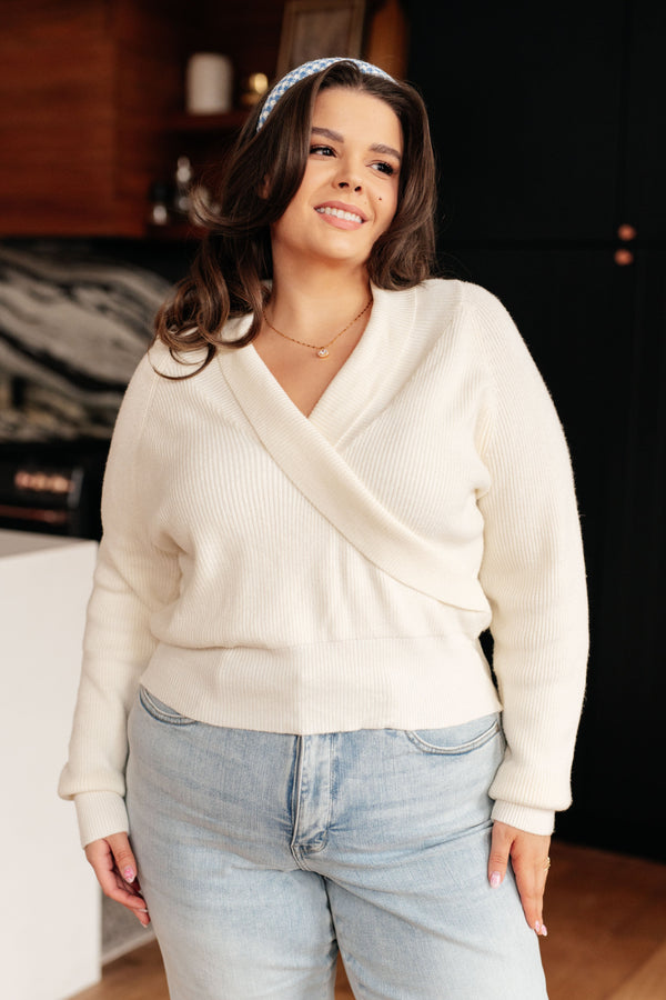 Woman wearing a cream sweater and light blue jeans indoors.