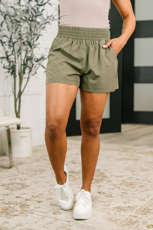Person wearing olive green shorts and white sneakers on a stone pavement.