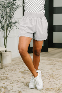 Person wearing light gray shorts and white sneakers on a patterned floor.