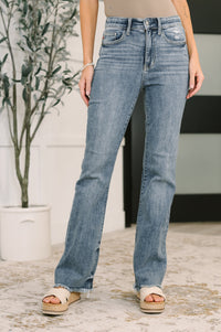 Person wearing blue jeans standing outdoors with a plant in the background