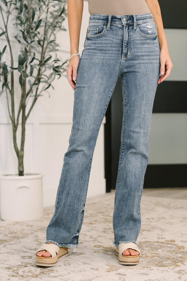 Person wearing blue jeans standing outdoors with a plant in the background