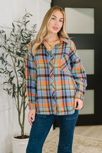 Woman wearing a plaid shirt and jeans standing indoors with a plant in the background