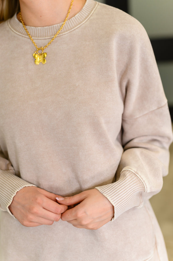 Person wearing a beige sweater and gold necklace with a pendant.