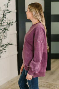 Woman wearing a purple sweatshirt standing outdoors with a plant in the foreground