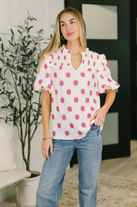 Woman wearing a white blouse with pink polka dots and blue jeans indoors.