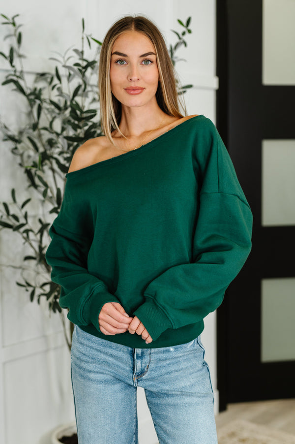 Woman wearing a green off-shoulder sweater and light blue jeans indoors.
