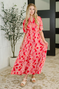 Woman wearing a red and white patterned dress standing indoors with a plant in the background.