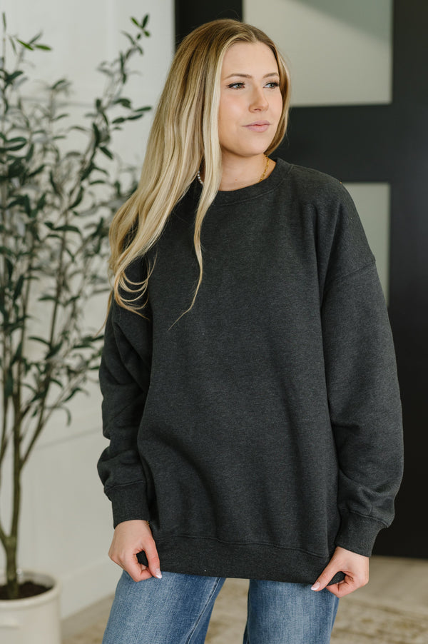 Woman wearing a dark gray sweatshirt in an indoor setting with a plant in the background