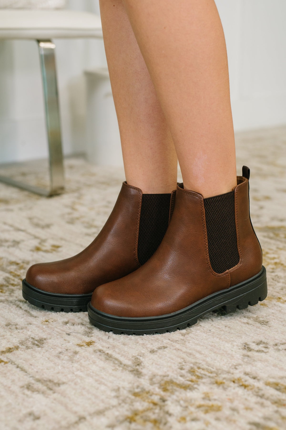 Brown Chelsea boots worn with black tights on a light-colored carpet.