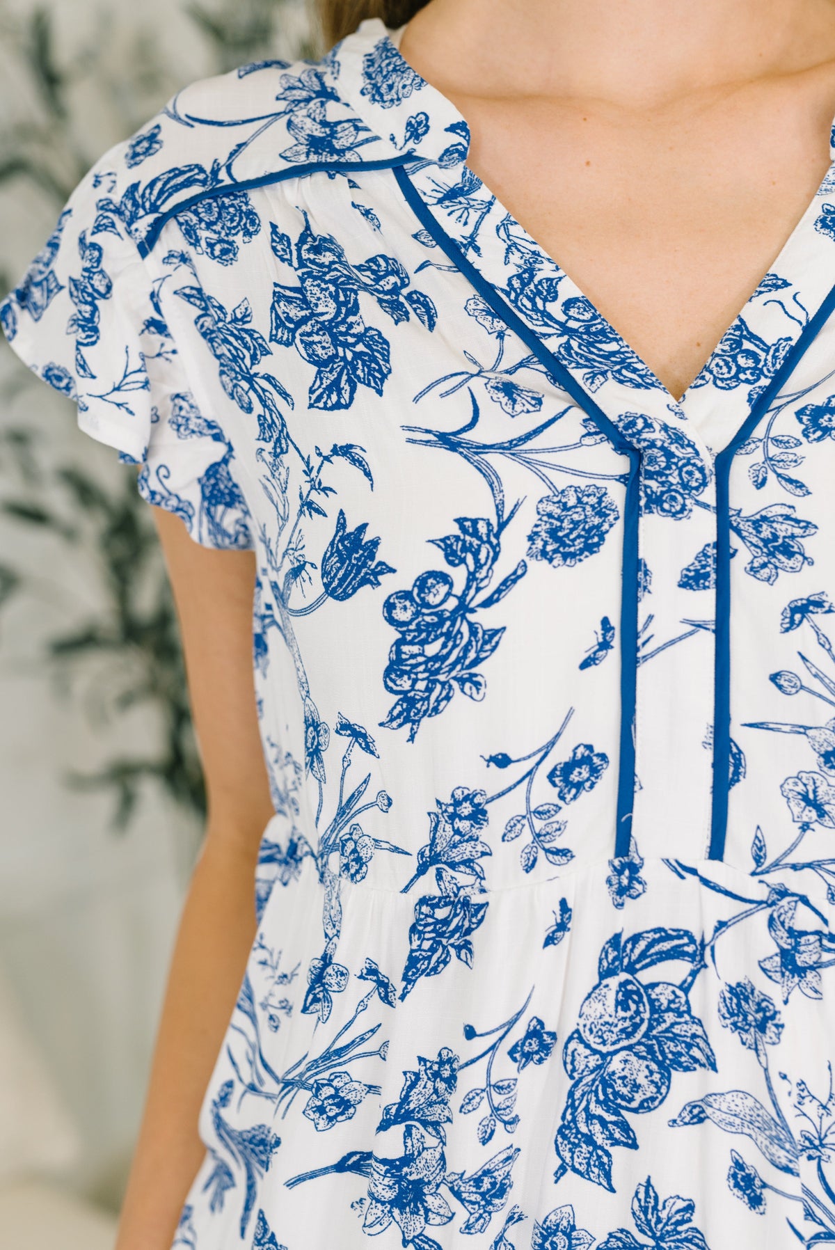 White top with blue floral pattern worn by a person, blurred background