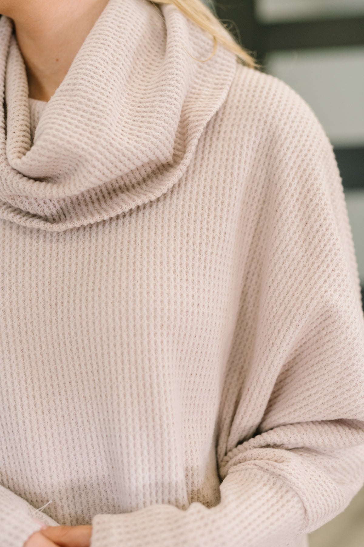 Close-up of a person wearing a beige knitted sweater with a blurred background