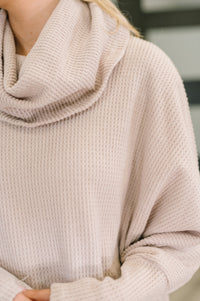 Close-up of a person wearing a beige knitted sweater with a blurred background