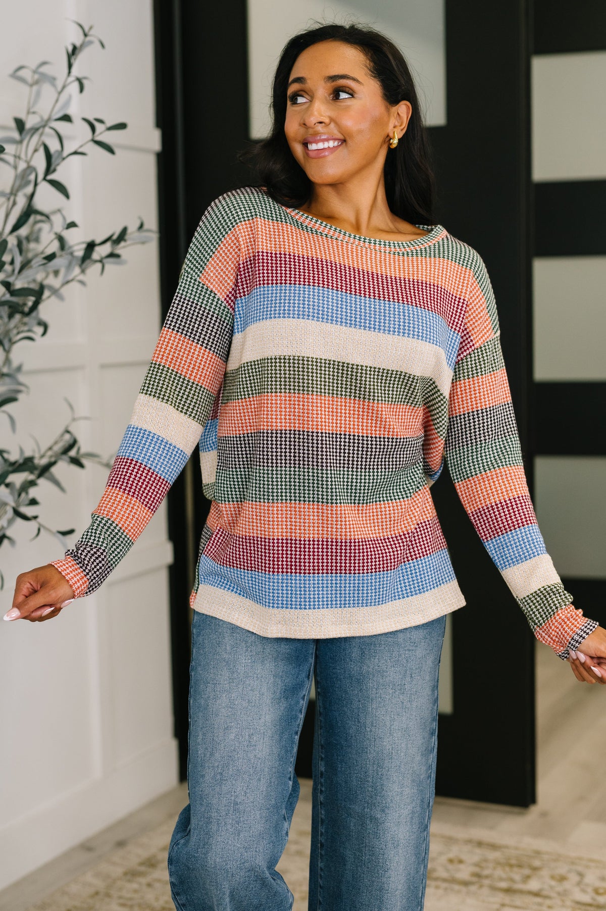 Woman wearing a colorful striped sweater and jeans indoors.