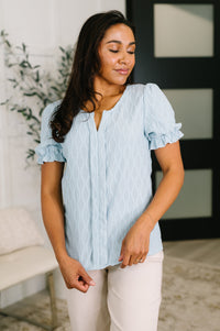 Woman wearing a light blue blouse with ruffled sleeves in an indoor setting.