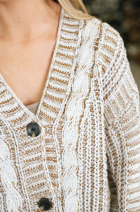 Close-up of a person wearing a cream and tan cable-knit cardigan with dark buttons.