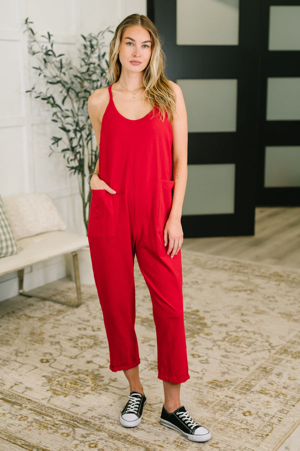Woman wearing a red jumpsuit standing in a room with a plant and bench.