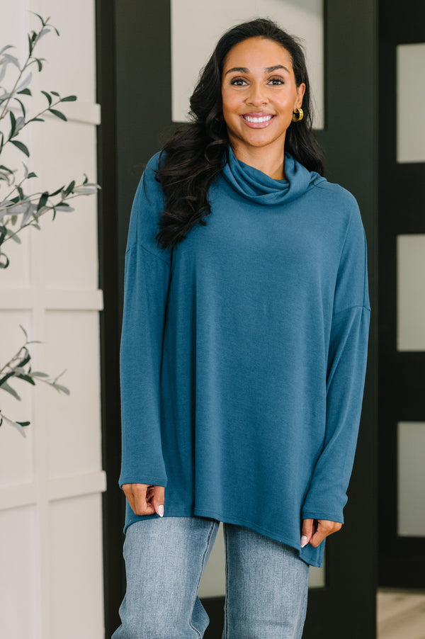 Woman wearing a teal long-sleeve top and jeans indoors.