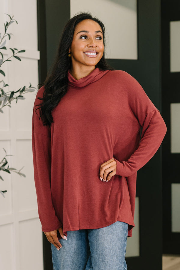 Woman wearing a rust-colored long-sleeve top and blue jeans indoors.