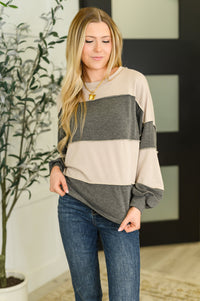 Woman wearing a beige and gray color-blocked sweater with blue jeans indoors.