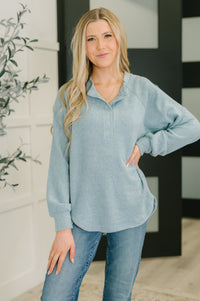 Woman wearing a light blue long-sleeve top and jeans standing indoors.