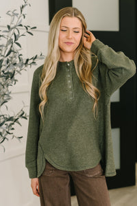 Woman wearing a green long-sleeve shirt with a blurred indoor background