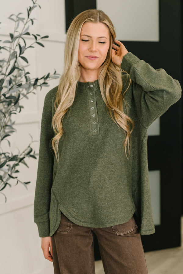 Woman wearing a green long-sleeve shirt with a blurred indoor background