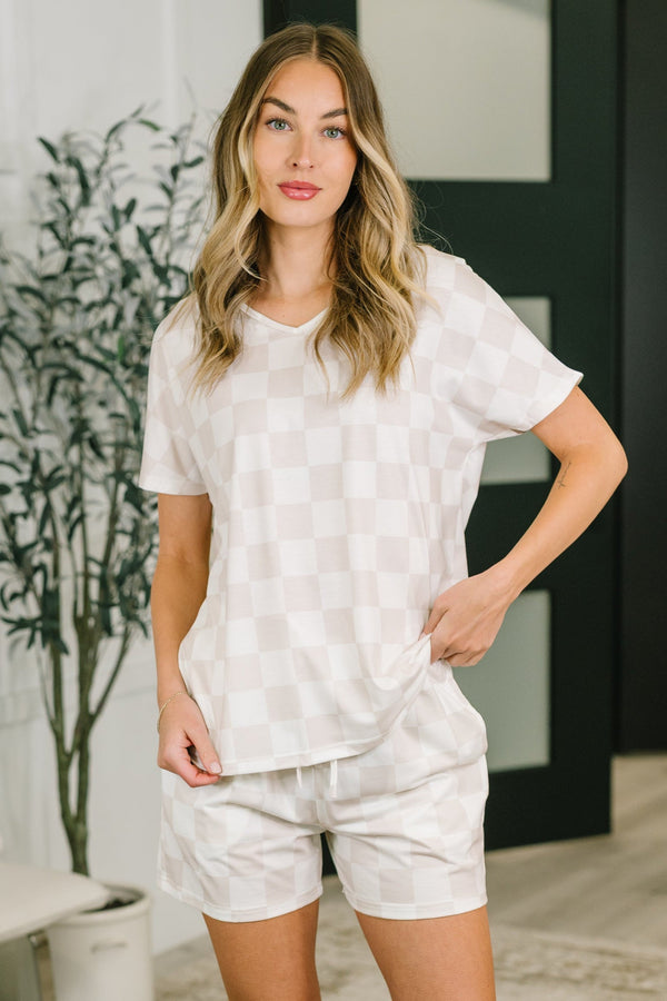 Woman wearing a white outfit standing in a room with a plant and furniture.