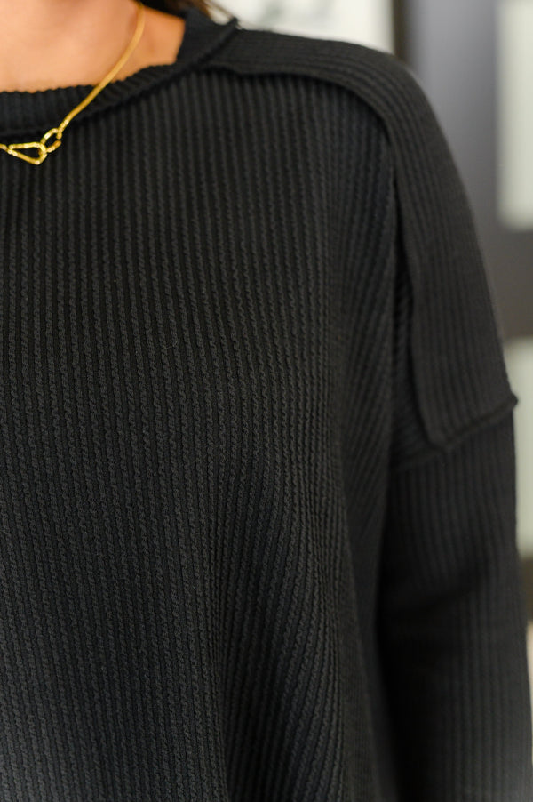 Black ribbed sweater with a gold necklace on a blurred background