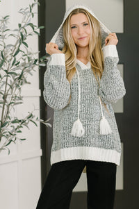 Woman wearing a gray and white hooded sweater with tassels in an indoor setting.