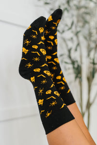 Black socks with yellow spider pattern held against a blurred natural background