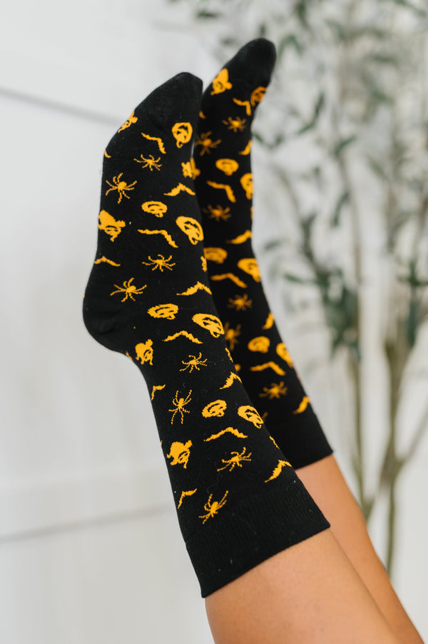 Black socks with yellow spider pattern held against a blurred natural background