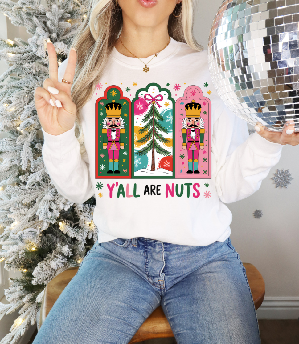 Person wearing a white sweatshirt with Christmas-themed designs and text, sitting in front of a decorated tree.