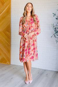 Woman wearing a floral dress standing against a white brick wall.