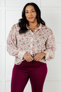 Woman wearing a floral blouse and burgundy pants against a white tiled wall